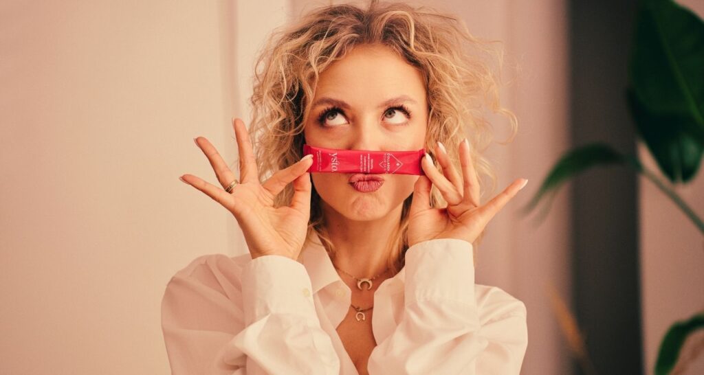 Kobieta trzyma saszetkę Ysto Collagen Your Skin i robi śmieszne miny.