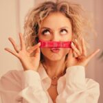 Kobieta trzyma saszetkę Ysto Collagen Your Skin i robi śmieszne miny.